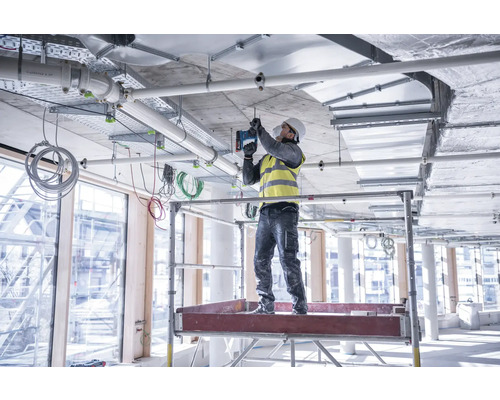 Ein Bauarbeiter steht auf einem Gerüst und befestigt eine Deckeninstallation.