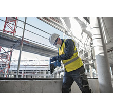 Ein Bauarbeiter bohrt mit einer Bohrmaschine in ein Betonstück auf einer Baustelle.