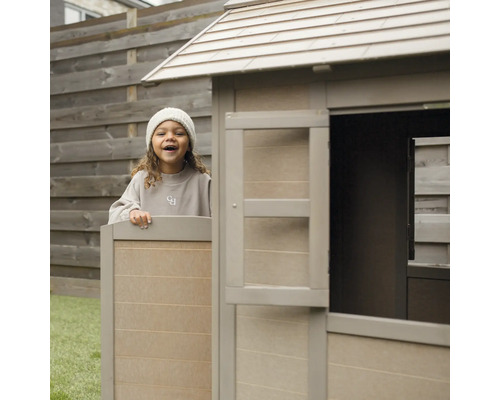 Kind spielt in einem Holzspielhaus im Garten.