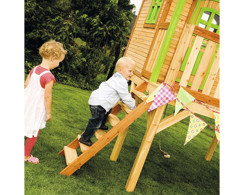 Ein Kind klettert auf einer Holzleiter zu einem Spielhaus im Garten, während ein anderes Kind zusieht.