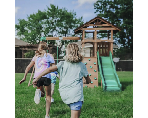 Kinder rennen auf einen Spielplatz mit Rutsche, Kletterwand und Schaukel zu