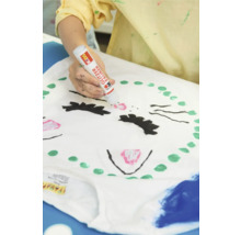 Eine Person bemalt ein T-Shirt mit einem Glitzerstift, um ein Katzengesicht zu gestalten.