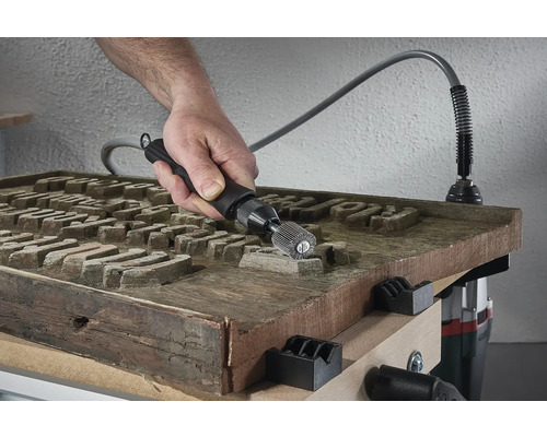 Hand mit Schleifwerkzeug bearbeitet Holzplatte mit Gravur auf einer Werkbank