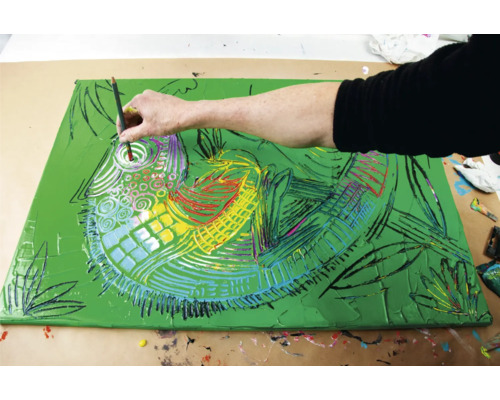 Eine Person malt mit Pinsel und Farbe auf einer Leinwand. Die Leinwand zeigt ein abstraktes Design.