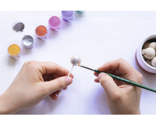 Hände bemalen Holzkugel mit Pinsel und Farbe