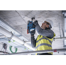 Ein Mann bohrt mit einer Schlagbohrmaschine in eine Betondecke, um eine Befestigung anzubringen.