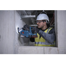 Ein Bauarbeiter mit Schutzhelm und Schutzbrille bohrt mit einem Bohrhammer ein Loch in eine Betonwand.