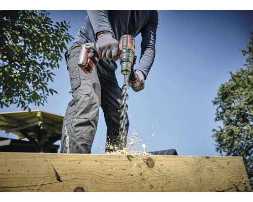 Eine Person bohrt mit einem Akku-Bohrschrauber ein Loch in ein Holzbrett, Holzspäne fliegen.