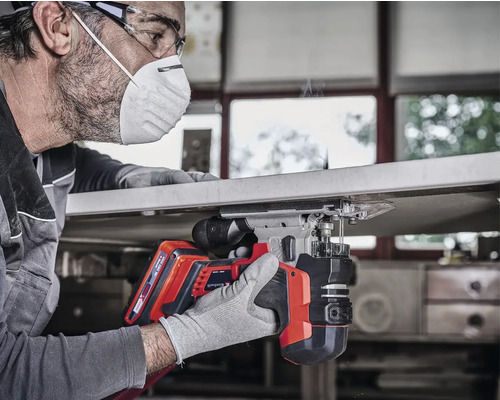 Ein Mann benutzt eine Akku-Stichsäge für Holzarbeiten, Schutzbrille und Gesichtsmaske sind getragen.