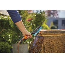 Eine Person reinigt einen Topf mit einer Bürste, die an einen Wasserschlauch angeschlossen ist, im Garten.