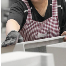 Eine Person mit karierter Schürze inspiziert eine weiße Keramiktoilette