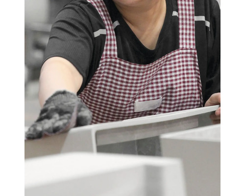 Eine Person mit Handschuhen und einer karierten Schürze inspiziert ein Produkt.