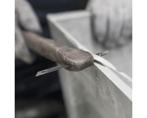 Dichtstoff wird mit einem Messer in einem Fensterrahmen entfernt.