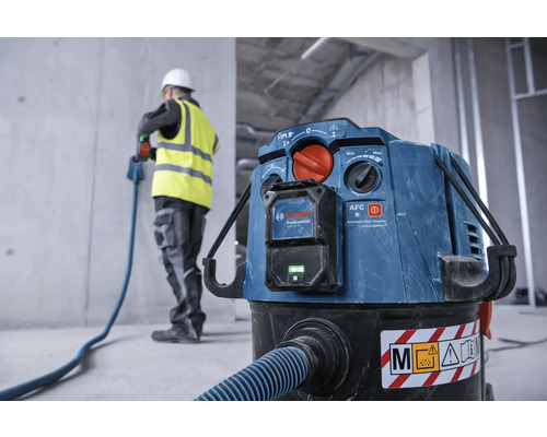 Industriestaubsauger mit Schlauch und Bauarbeiter im Hintergrund