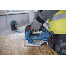 Eine Person sägt mit einer Stichsäge ein Loch in ein Holzbrett. Im Hintergrund ist ein Staubsauger zu sehen.