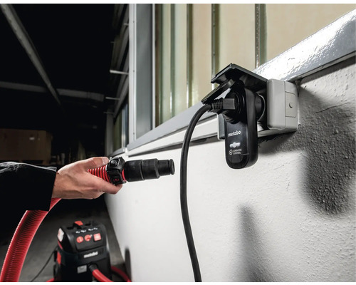 Eine Person schliesst einen Staubsaugerschlauch an eine Metabo Cordless Control Steckdose an.
