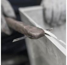 Eine Hand mit Handschuh bearbeitet eine Fensterdichtung mit einem Messer.