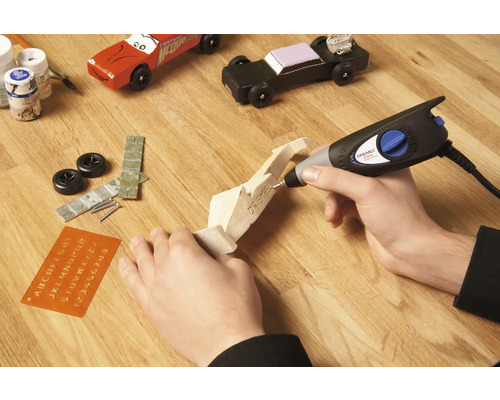 Handwerksszene mit Dremel Multifunktionswerkzeug, Holzmodellauto und Zubehör auf Holztisch.