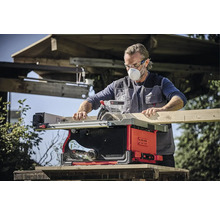 Mann mit Schutzmaske und Schutzbrille beim Sägen eines Holzbretts mit einer Einhell Tischkreissäge