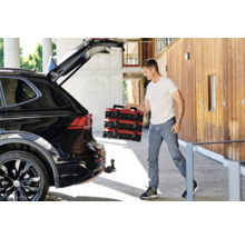 Mann lädt rote Werkzeugkoffer aus einem schwarzen Auto