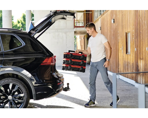 Mann lädt rote Werkzeugkoffer aus einem schwarzen Auto