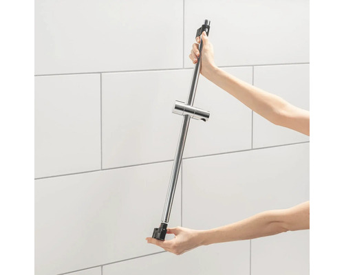 Eine Person hält eine Duschstange mit einem Brausehalter vor einer gefliesten Wand.