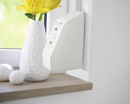 Fensterdekoration mit Rollladensteuerung neben einer Vase mit gelben Lilien