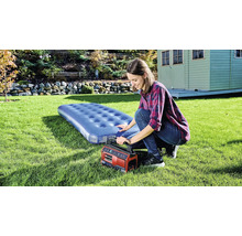 Frau pumpt Luftmatratze mit einer elektrischen Pumpe im Garten auf.