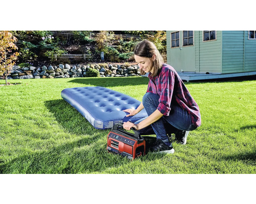 Frau pumpt Luftmatratze mit einer elektrischen Pumpe im Garten auf.