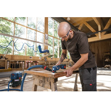 Ein Handwerker benutzt einen Multifunktionsschleifer zum Schleifen eines Holzrahmens mit Staubabsaugung in einer Werkstatt.