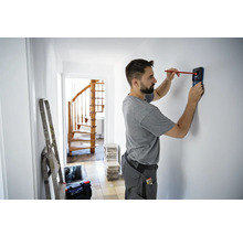 Mann benutzt einen Detektor zum Auffinden von Objekten in einer Wand in einem Haus.