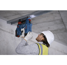 Ein Arbeiter befestigt eine Metallschiene mit einem Bolzenschussgerät an einer Betondecke.