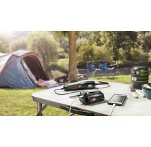 Campingszene mit Tisch, Zelt, Kochgeschirr, Ladegerät, Gartenschere und Smartphone