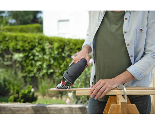 Eine Frau schneidet mit einer Stichsäge ein Holzbrett im Freien.