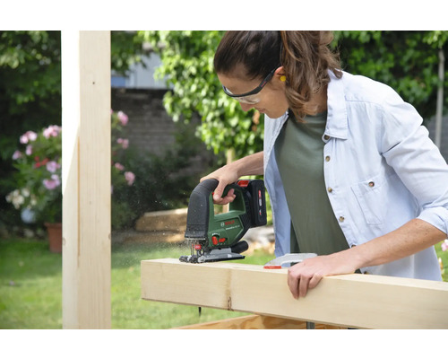 Eine Frau sägt ein Holzbrett mit einer Stichsäge im Garten.