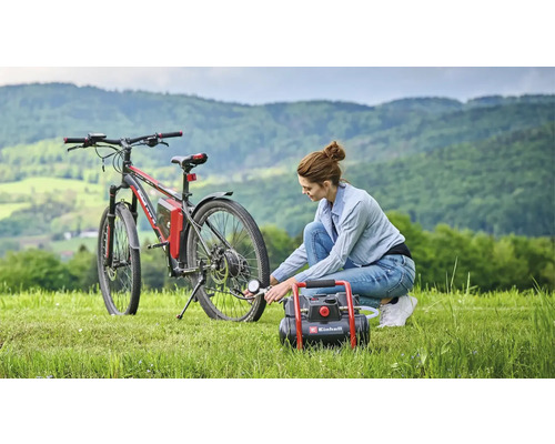 Frau pumpt Fahrradreifen mit einem Einhell Kompressor auf einer Wiese vor einer Hügellandschaft auf