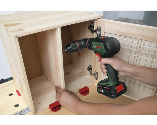 Eine Person bohrt mit einem Akku-Bohrschrauber ein Holzmöbel zusammen.