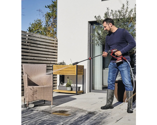 Ein Mann reinigt mit einem Hochdruckreiniger eine Terrasse im Außenbereich.