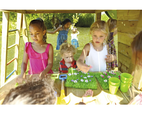 Kinder spielen in einem Spielhaus mit Sandkastentisch, Bechern und Gartengeräten.