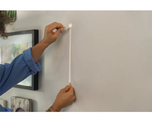 Frau befestigt eine Bilderleiste an der Wand.