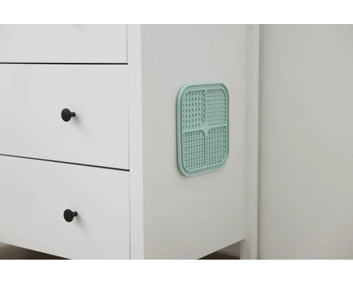 Detailansicht eines weißen Badezimmerschranks mit einem türkisfarbenen Lüftungsgitter.