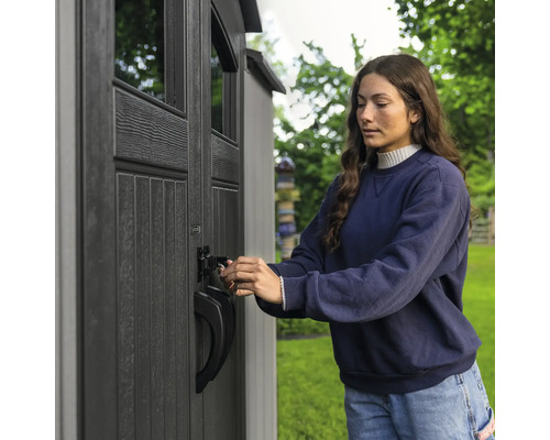Eine Frau schliesst eine Gartengerät-Aufbewahrung ab.