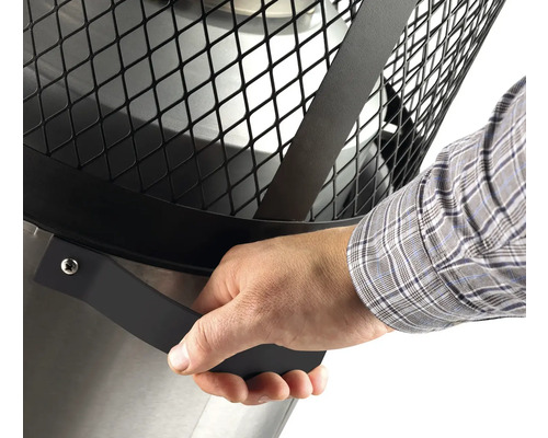 Detailansicht einer Feuerstelle mit Hand am Griff des Schutzgitters.