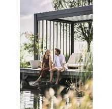Paar sitzt auf einem Holzsteg am Wasser unter einer Pergola. Gartengestaltung mit Loungemöbeln und Bepflanzung.