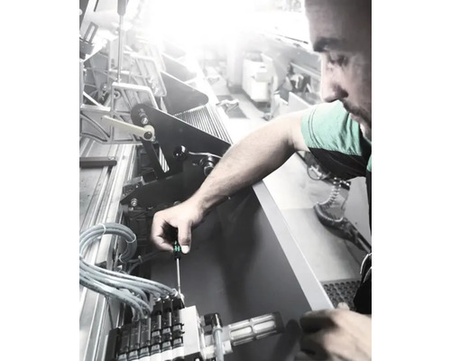 Ein Mann, der eine Maschine mit einem Schraubendreher repariert.