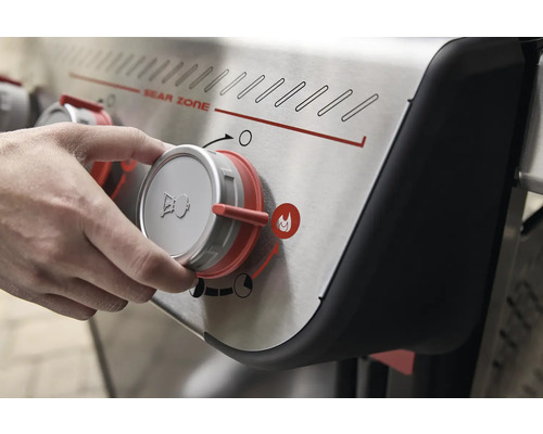 Nahaufnahme eines Gasgrills mit Drehknopf in der Hand, der die Sear Zone einstellt.