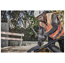 Ein Bauarbeiter mit Helm und Schutzweste bedient eine Rüttelplatte mit einer Kette an einer Baustelle.