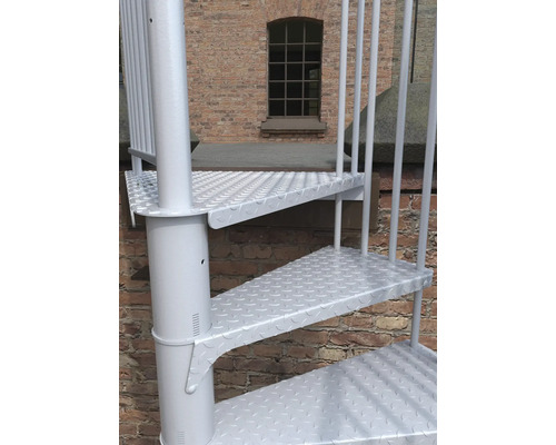Detailaufnahme einer weißen Wendeltreppe vor einer Backsteinmauer.