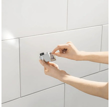 Nahaufnahme einer Hand, die einen verchromten Thermostat-Druckknopf mit Zahlen auf einer gefliesten Wand bedient