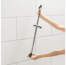 Eine Person hält eine Duschstange mit Duschkopfhalter vor einer gefliesten Wand.